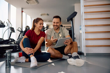 Happy sportswoman and her personal coach planning exercise class on touchpad in  gym.