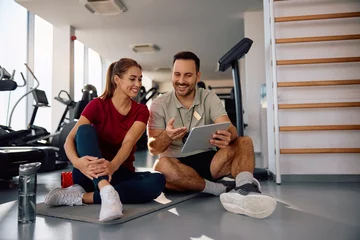 Fotobehang Persoonlijk Happy sportswoman and her personal coach planning exercise class on touchpad in  gym.  © Drazen