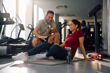 Happy sportswoman doing warm up exercises while coach's assistance in  gym.