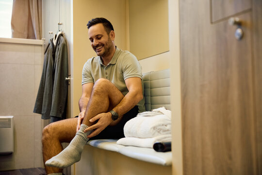 Happy man getting dressed for sports training at gym's locker room.