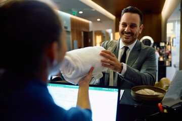 Happy businessman receiving clean towels while checking in at gym reception desk.