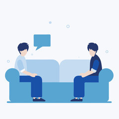 Two men are sitting on a couch, one of them is talking to the other. The couch is blue and the men are wearing blue shirts. Scene is casual and friendly, as the two men are having a conversation