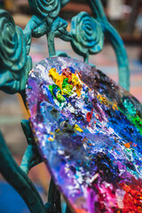 Closeup of messy, colorful artist's palette resting on turquoise chair