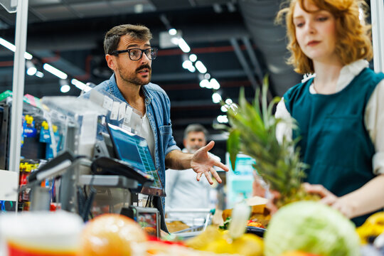 Customer complaining to cashier about prices in supermarket checkout line