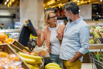 Senior couple weighing oranges at supermarket self service scale