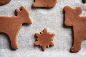 Shapes made of raw pastry dough on a sheet of baking paper - gingerbread Christmas cookies