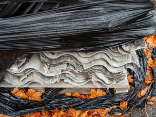Eternit sheets dismantled from the roof, placed on pallets and wrapped in black foil.