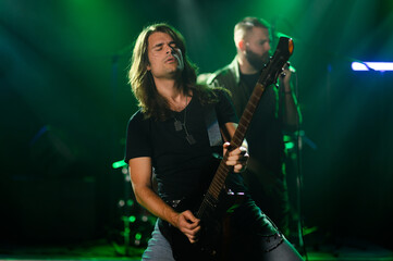 Fototapeta premium Guitarist performing live on stage with band in green lights