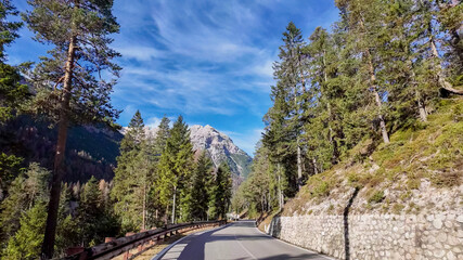 Scenic landscape of a winding Alpine road surrounded by lush pine trees and majestic mountains, ideal for adventure travel Dolomite Alps, Dolomites