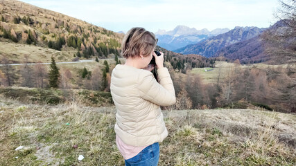 A Caucasian woman captures the scenic beauty of autumn in a mountainous landscape, highlighting the concept of nature photography