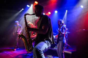 Saxophonist performing with band on stage under colorful lights