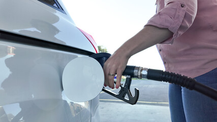 A person refuels a car at a gas station, highlighting the concept of rising fuel costs and travel preparation