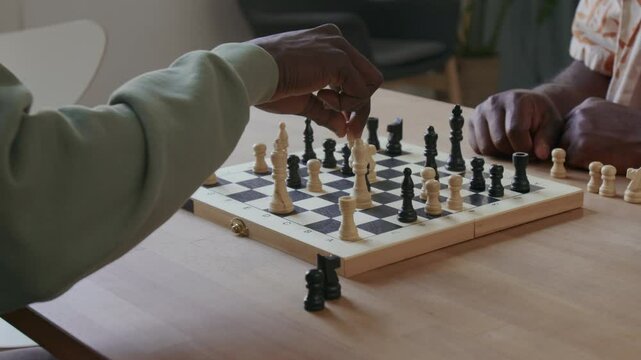Close up view of hands of unrecognizable Black man taking enemy pawn with bishop while playing chess game with friend at home