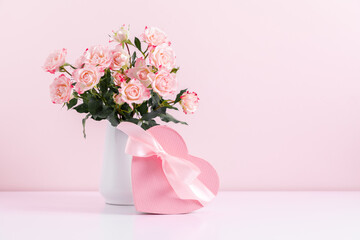 Beautiful bouquet flowers pink roses in vase and  gift box with satin bow on pastel pink background table. Birthday, Wedding, Mother's Day, Valentine's day, Women's Day. Front view