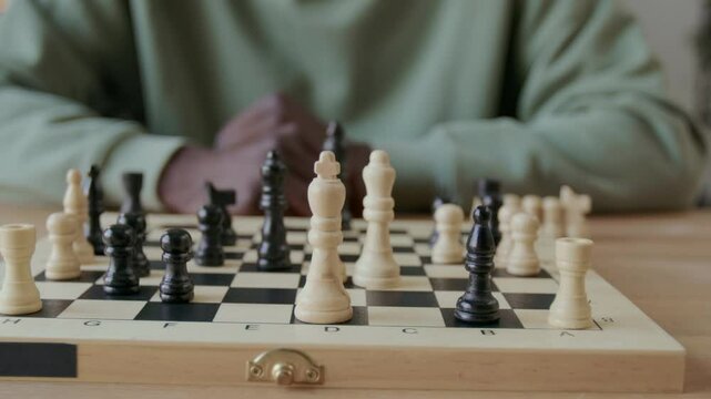 Close-up view of hand of unrecognizable Black man moving bishop on chessboard while practicing solo at home