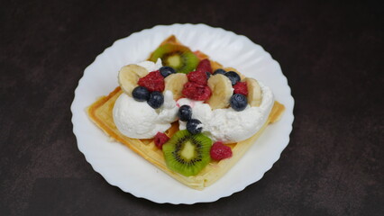 Waffles with whipped cream, blueberries, bananas, raspberries, and kiwi