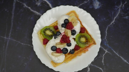 Waffles with whipped cream, blueberries, bananas, raspberries, and kiwi