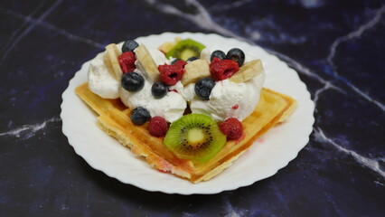 Waffles with whipped cream, blueberries, bananas, raspberries, and kiwi