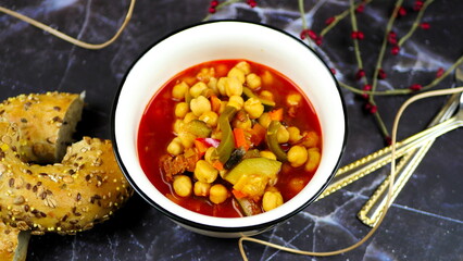 A dish of chickpeas, peppers, carrots and other vegetables with a whole grain roll