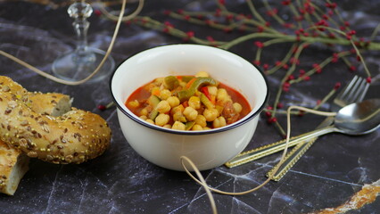 A dish of chickpeas, peppers, carrots and other vegetables with a whole grain roll
