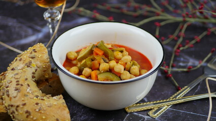 A dish of chickpeas, peppers, carrots and other vegetables with a whole grain roll