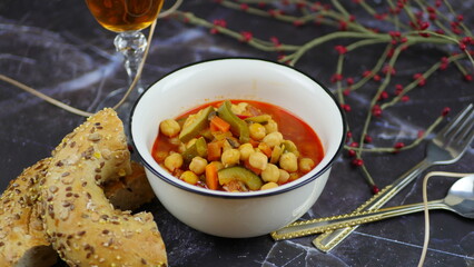 A dish of chickpeas, peppers, carrots and other vegetables with a whole grain roll