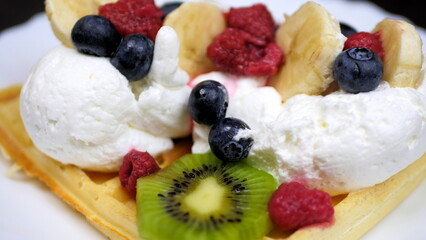 Waffles with whipped cream, blueberries, bananas, raspberries, and kiwi