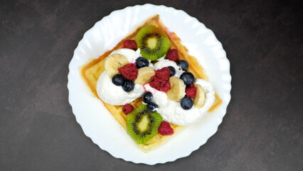 Waffles with whipped cream, blueberries, bananas, raspberries, and kiwi