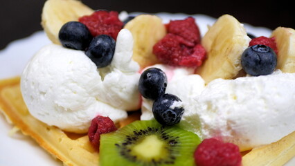 Waffles with whipped cream, blueberries, bananas, raspberries, and kiwi
