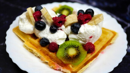 Waffles with whipped cream, blueberries, bananas, raspberries, and kiwi