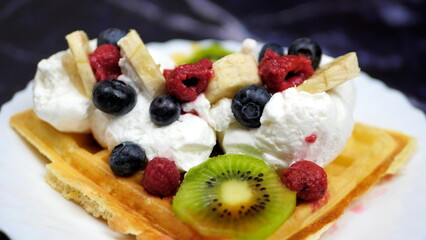 Waffles with whipped cream, blueberries, bananas, raspberries, and kiwi