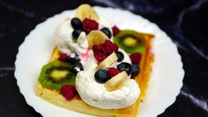 Waffles with whipped cream, blueberries, bananas, raspberries, and kiwi