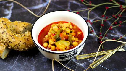 Dish with chickpeas, peppers, carrots and other vegetables with a whole grain roll and a glass of wine
