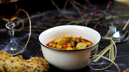 Dish with chickpeas, peppers, carrots and other vegetables with a whole grain roll and a glass of wine
