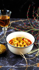 Dish with chickpeas, peppers, carrots and other vegetables with a whole grain roll and a glass of wine
