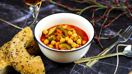 Dish with chickpeas, peppers, carrots and other vegetables with a whole grain roll and a glass of wine
