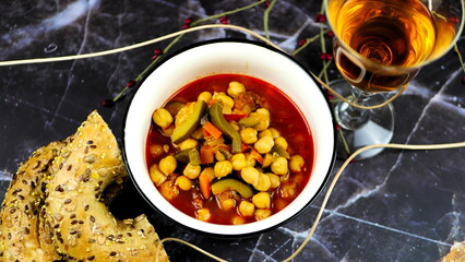 Fototapeta premium Dish with chickpeas, peppers, carrots and other vegetables with a whole grain roll and a glass of wine 