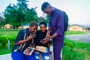 three African college students standing outdoors looking at phone smiling after class