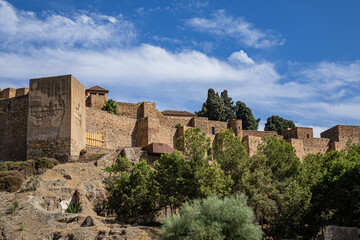 Fototapeta premium Scenic view of ancient ruins of Malaga Roman Theater (El Teatro Romano, I century BC) with historic Roman semi-circular seating at foot of famous Alcazaba fortress. Malaga, Andalusia, Spain.