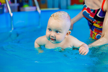 A baby learns to swim in a pool with a trainer. Children's pool. Swimming courses for children.