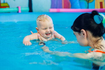 A little boy learns to swim in a pool with a female coach. Baby swims in the pool.