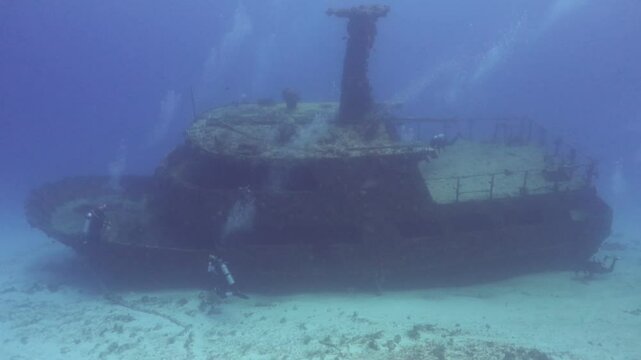 panor&aacute;mica de un barco hundido en el fondo del mar con buzos explorando a su alrededor.