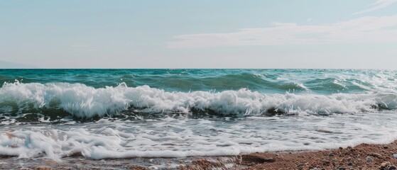 Fototapeta premium Waves gently lap against the shore under a clear blue sky, capturing the soothing essence of the ocean on a sunny day.