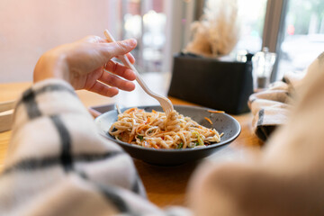 A woman enjoying a delicious bowl of wok noodles in a cozy café during a sunny afternoon
