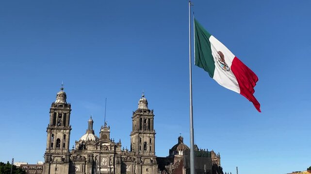 Mexican flag flutters in front of the Metropolitan Cathedral located in Zocalo plaza, downtown Mexico City, Mexico.