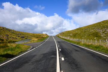 Two lane paved road in Wales leading to ridge with rugged hillside