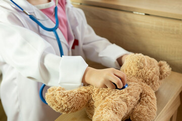 little child, blonde girl 4 years old plays with toy, little doctor treating teddy bear, happy...