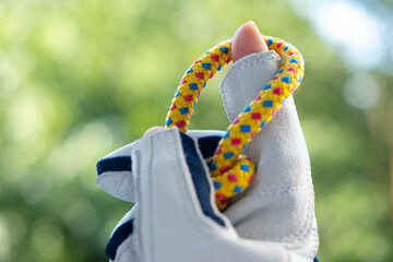 Close-up gloved hand holding colorful braided rope against blurred green background. Sailing or...