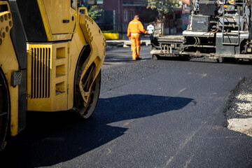 Road construction crew laying asphalt on a sunny day in an urban area with yellow machinery working...