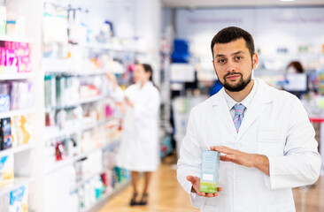 Portrait of european man druggist in lab coat standing in drugstore with drug package.